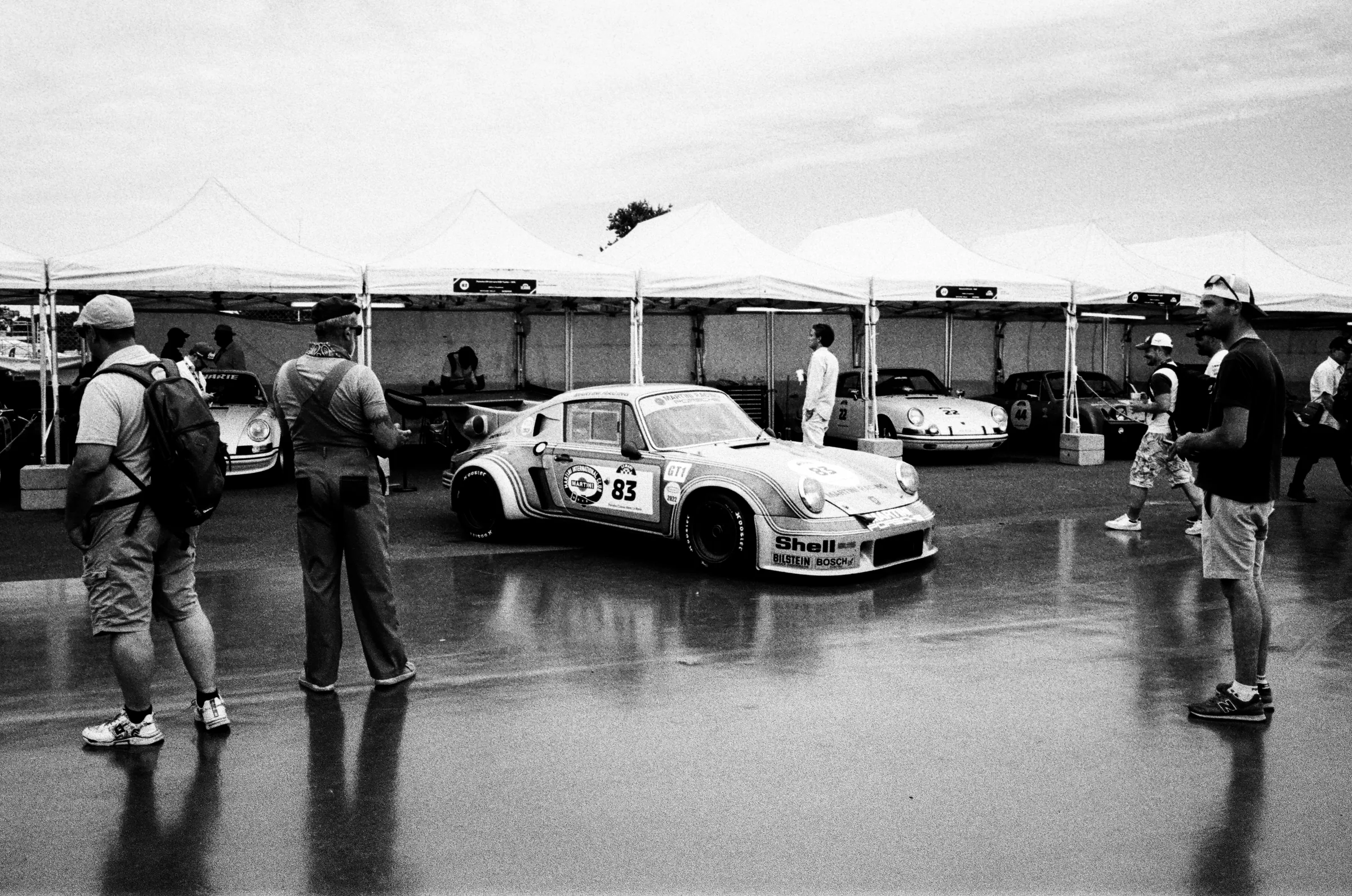 A vintage racing car in a paddock under tents, in black and white, framed inside the Second View viewfinder